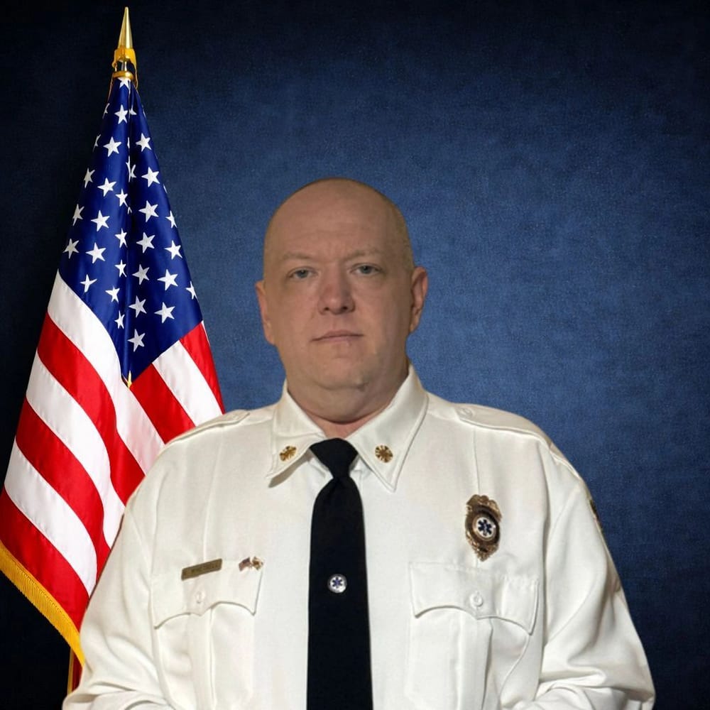 Chief Scott Whetsell in dress uniform in front of an American flag
